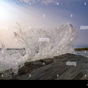 A wave crashes dramatically against coastal rocks, sending water spray into the air.