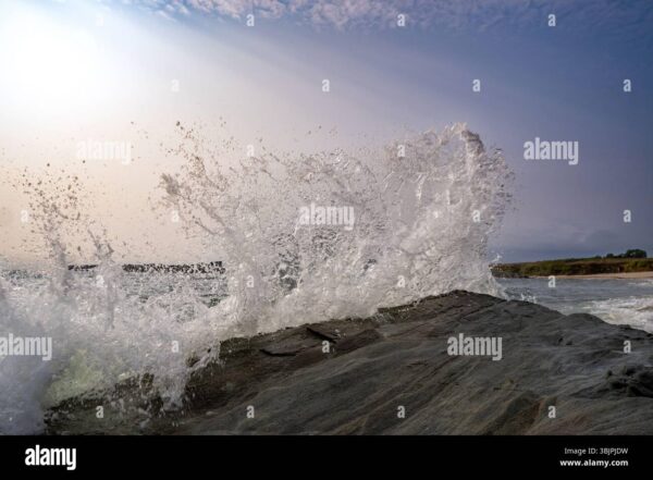 A wave crashes dramatically against coastal rocks, sending water spray into the air.