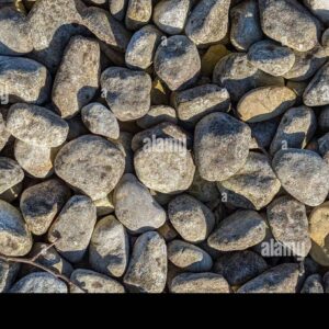Close-up view of a pile of natural gray river stones with sunlight and shadows creating texture.