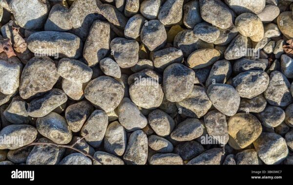 Close-up view of a pile of natural gray river stones with sunlight and shadows creating texture.