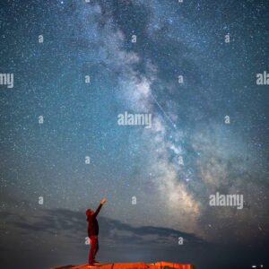 Person standing on a concrete structure, pointing at the Milky Way galaxy in the night sky.