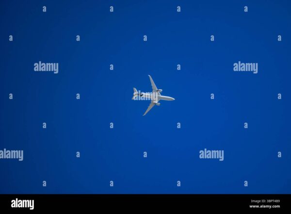 Commercial airplane flying across a clear blue sky, viewed from below.