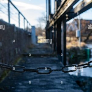 Close-up of a metal chain blocking access to an industrial walkway, symbolizing restriction or security.