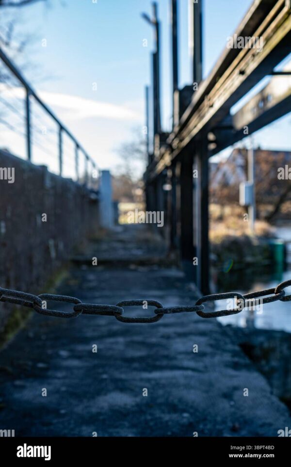 Close-up of a metal chain blocking access to an industrial walkway, symbolizing restriction or security.